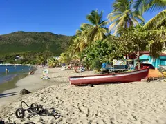 Colorful Small Fishing Boats On Sandy Beach In Martinique With Palm Trees And Mountains In Backdrop