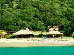 Deserted Beach In The Grenadines With Dense Forest In Backdrop And Straw Huts Near Water