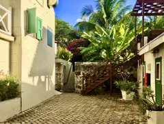 House With Green Shatters On A Court With Bougainvillae And Palm Trees And Ground Layers With Brick Stone